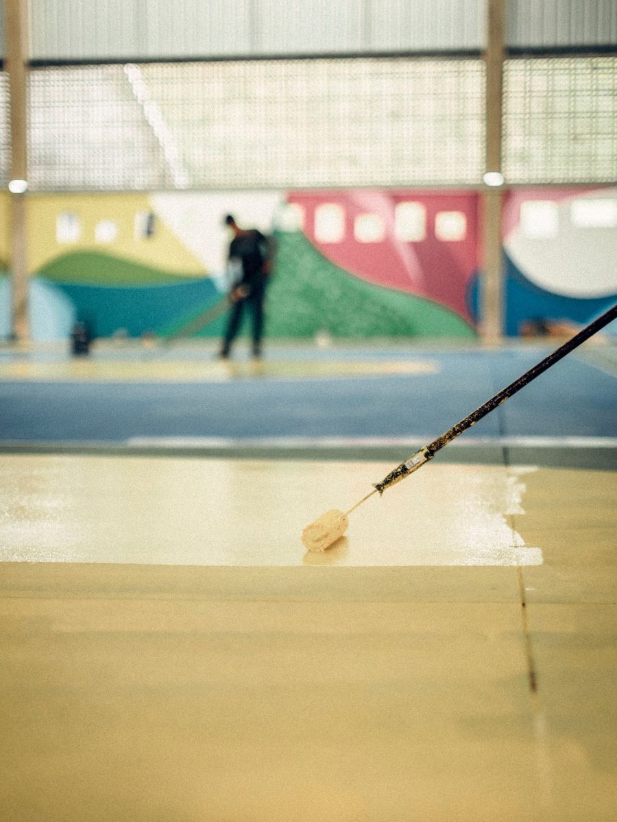Installer pulling a fresh floor coating across a prepared slab with a long-handled squeegee