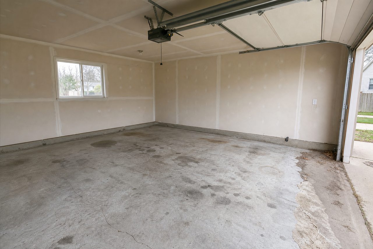 Empty two-car garage with a cracked, stained bare concrete floor before coating