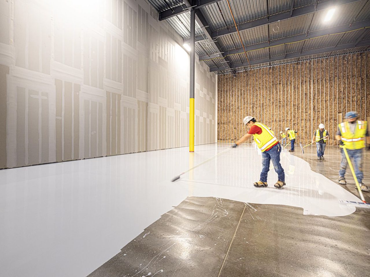 Crew in high-visibility vests installing an epoxy floor coating across a prepared concrete slab